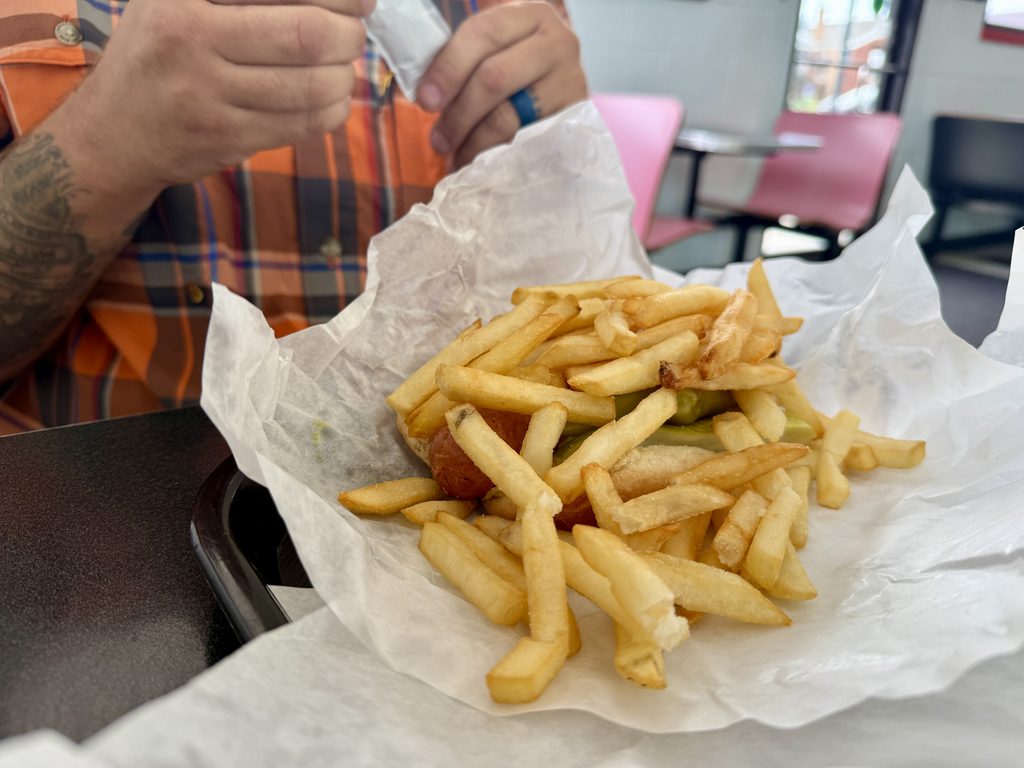 man sitting in front of a hotdog that is piled on top with french fries