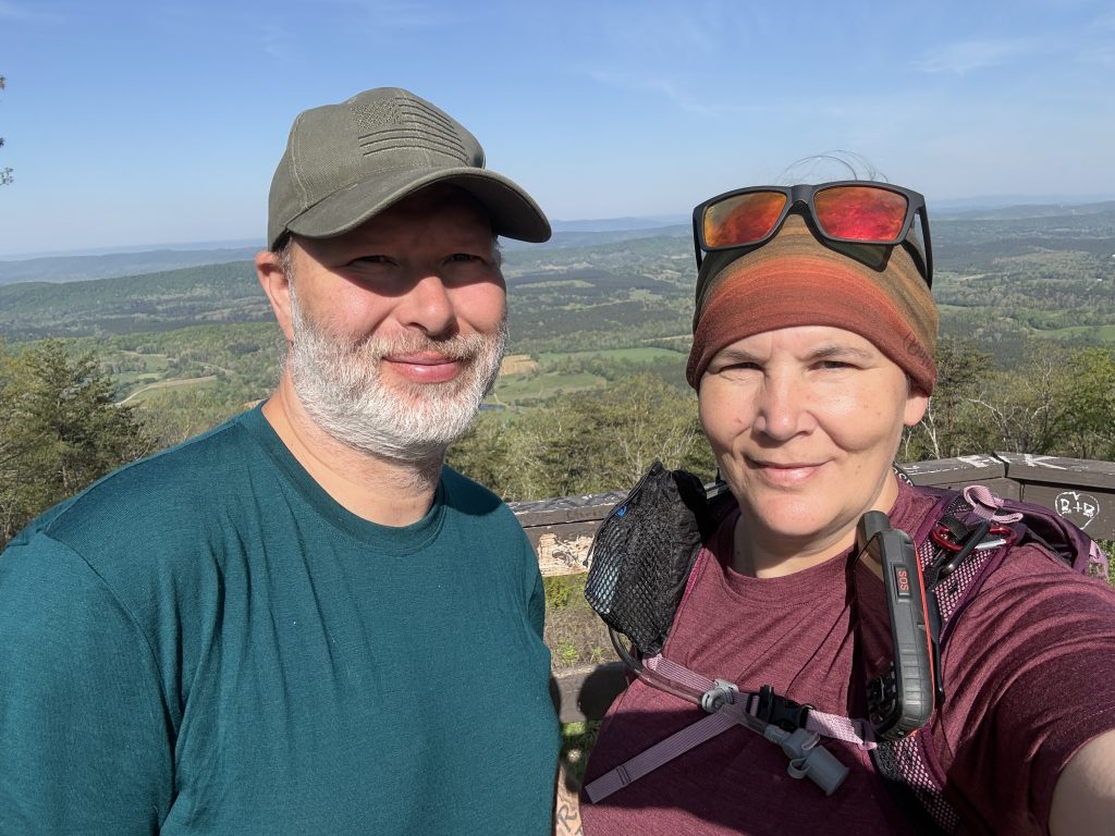 nutty hiker and suspenders standing at an overlook that looks over the valley below