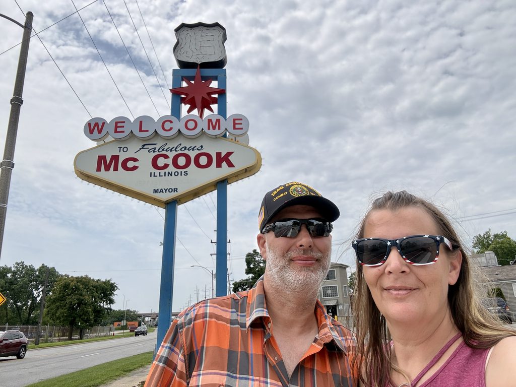 couple standing in from of the welcome to Mc Cook sign on Route 66