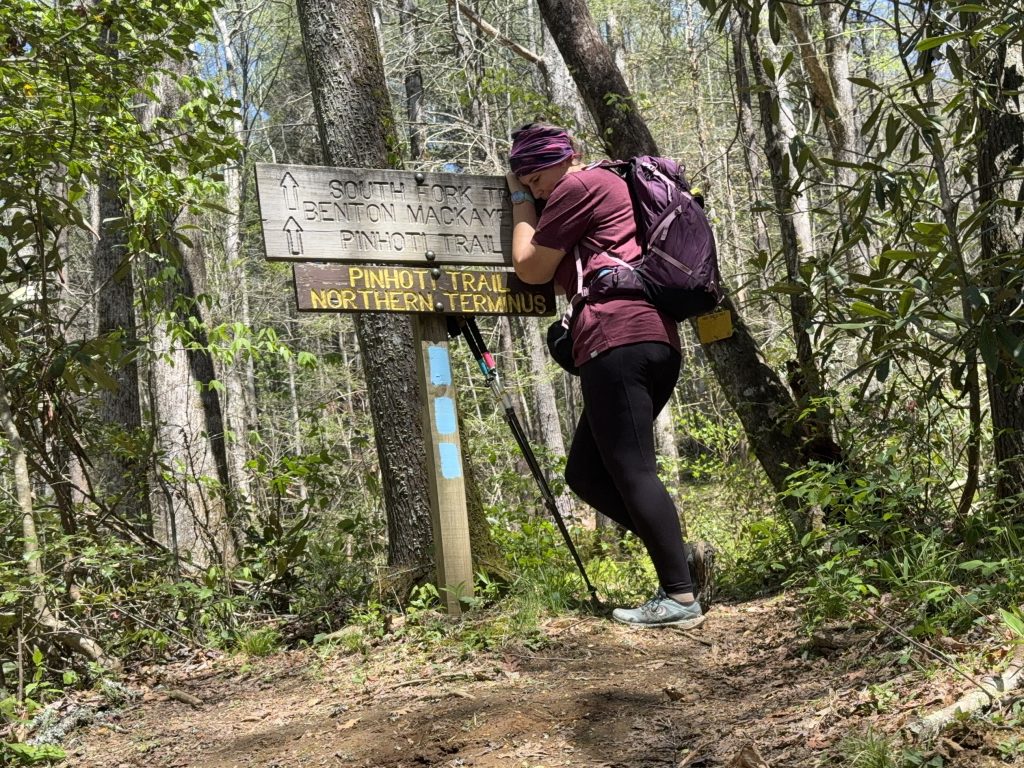 person hugging a sign for the pinhoti trail northern terminus