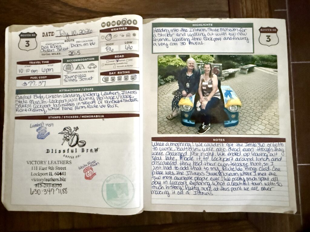 Open travel journal with handwritten notes, stamps, and memorabilia covering a Route 66 road trip dated July 10, 2023. The journal details daily highlights, stops, and expenses, and features a color photo of two women sitting on a colorful bench made from vintage car parts, with bushes and stone benches in the background.