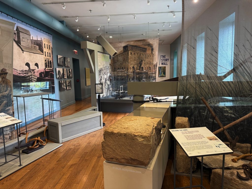 Interior of the Gaylord Building museum, featuring educational exhibits, historic artifacts, and informational panels about the Illinois & Michigan Canal, set against wood floors and large wall graphics.