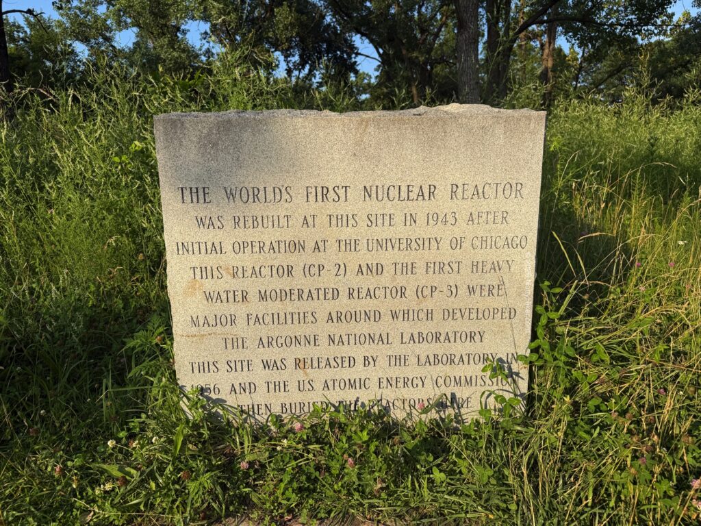 Stone monument in tall grass with an inscription describing the world’s first nuclear reactor, rebuilt at Site A in 1943.