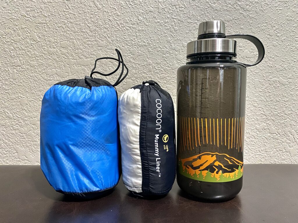 Comparing sleeping bag liner sizes next to a water bottle